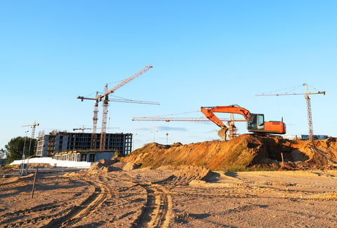Construction site with tower cranes on residential buildings and excavator on groundwork