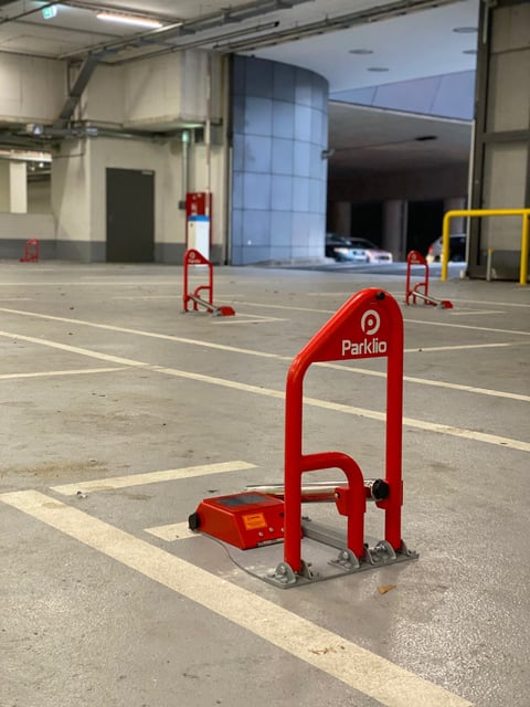 Red Parklio parking barrier on concrete parking garage floor with additional barriers visible in background
