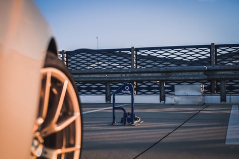 Close-up of a car wheel in sharp focus with a parking structure and loading dock blurred in the background.