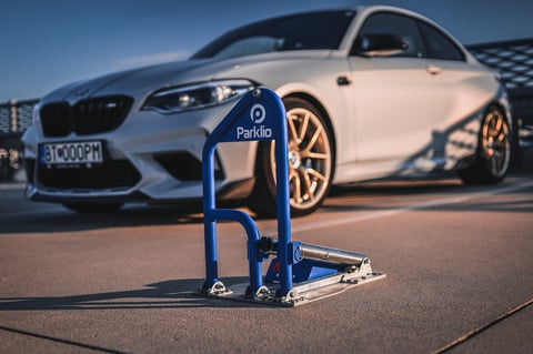 Blue parking lock device in foreground with white luxury sports car blurred in background on parking lot